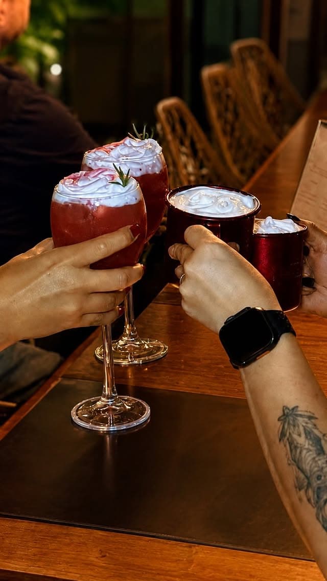 Amigos brindando com drinks de frutas vermelhas e canecas esmaltadas na mesa de madeira