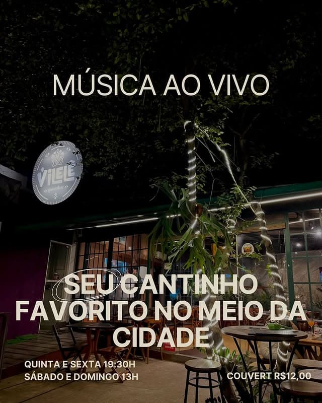 Fachada do Vilelê à noite, com placa redonda iluminada e luzes entre as árvores