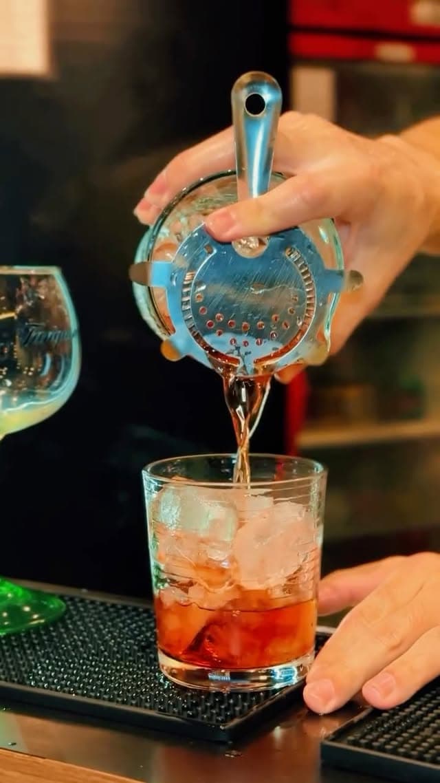 Bartender coando um negroni no copo baixo com gelo, no balcão do bar