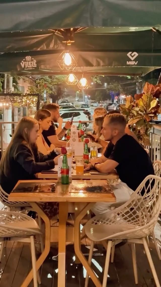 Varanda do Vilelê à noite, com toldos verdes, luminárias acesas e mesas ocupadas na calçada da Joaquim Lírio